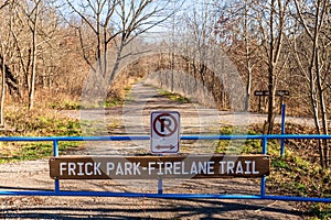 A no parking sign on a gate with a wooden sign for the Frick Park Firelane Trail in Frick Park in Pittsburgh, Pennsylvania, USA