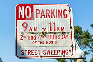 No parking sign from nine to eleven for street sweeping in urban or suburban area with foliage and tree with blue sky