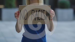 NO RACISM on cardboard poster in hands of female protester activist. Stop Racism concept, No Racism. Rallies against