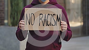 NO RACISM on a cardboard poster in the hands of male protester activist. Closeup of poster and hand. Stop Racism concept