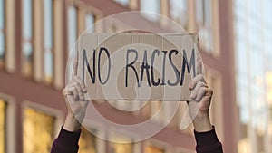 NO RACISM on cardboard poster in hands of male protester activist. Stop Racism concept, No Racism. Rallies against