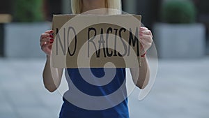 NO RACISM on a cardboard poster in the hands of white female protester activist. Closeup of poster and hand. Rallies