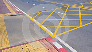 No stopping yellow crisscross zone traffic sign on asphalt road surface with yellow tactile paving line on sidewalk