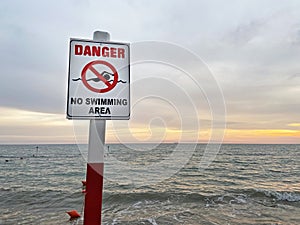 No Swimming area sign post plaque on sea water background. No swim area signage pillar, mounted on the shore sea beach