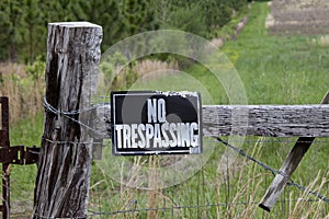 No trespassing sign on weathered fence post in front of a green