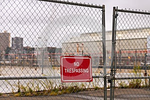 No trespassing sing hanged on an wire fence in front of a dockyard.