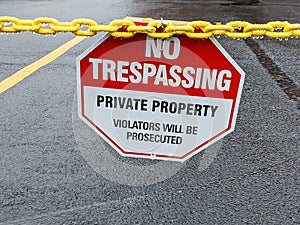 No Trespassing Warning Sign On Yellow Chain Blocking Road Entrance