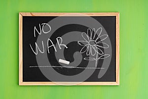 No war is written on the black board and a flower is drawn, next to it is a crayon with which the child drew