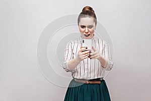 No way! Portrait of shocked attractive blogger young woman wearing in striped shirt standing, using smartphone and watching video