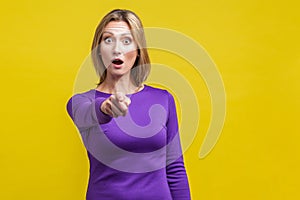 No way, that`s you! Portrait of wondered woman in tight purple dress pointing at camera.  on yellow background