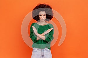 No way. Serious woman with Afro hairstyle wearing green sweater standing with crossed hands, showing