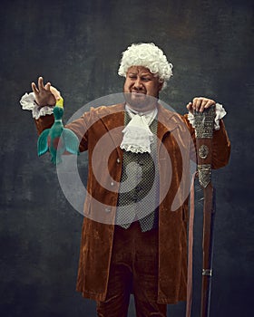Nobleman, medieval royal person in vintage hunting clothing with old gun isolated over dark background. Art, fashion