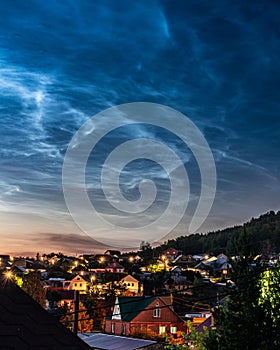 Noctilucent cliuds in the night sky above mountain village in summer photo