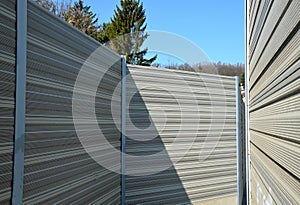 Noise barrier made of metal perforated sheet metal slats. gray and silver protective fencing separates housing from a busy noisy r