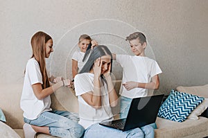 Noisy children distract mothers from working at the computer. annoyed mom holds her head