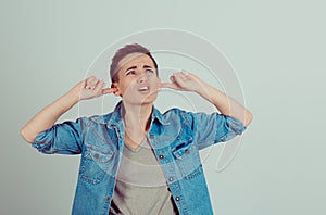 Noisy neighbors. Portrait of a boy alike woman girl plugging the ears looking up