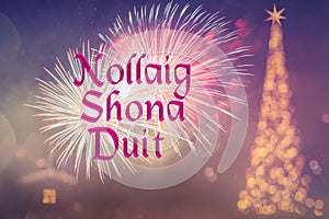 Nollaig Shona Duit means Merry Christmas in Irish. Blurred background of decorated Christmas tree with golden lights. Fireworks.