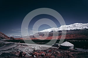 Nomadâ€™s tent, snow-capped mountains in the distance, blue sky and red rock mountains, a grassland in the valley