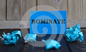 NOMINATE - words on blue paper on a dark wooden background with crumpled pieces of paper photo