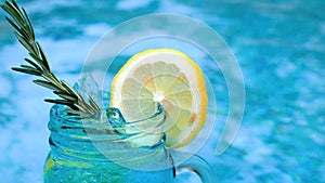 Non-alcoholic blue cocktail with rosemary and lemon slice near swimming pool