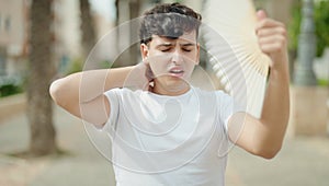 Non binary man using handfan suffering for hot at park