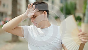 Non binary man using handfan suffering for hot at park