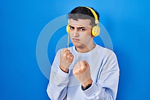 Non binary person listening to music using headphones ready to fight with fist defense gesture, angry and upset face, afraid of