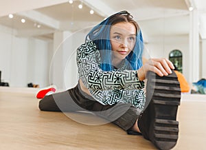 Non-binary person stretching leg wide on dance studio floor, reaching boot sole near studio mirror photo
