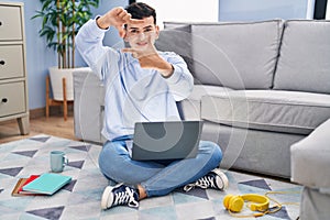 Non binary person studying using computer laptop sitting on the floor smiling making frame with hands and fingers with happy face
