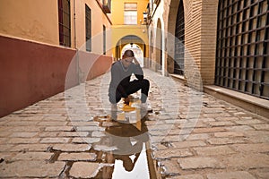 Non-binary person, young and South American, heavily make up crouched in the middle of a street, hand on his head worriedly