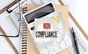 NON COMPLIANCE word on sticky with clipboard and notebook, business concept photo