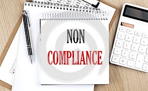 NON COMPLIANCE is written in white notepad near a calculator, clipboard and pen. Business concept photo