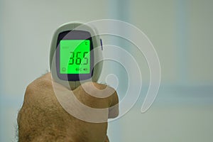 Non contact infrared forehead digital thermometer held by a young man with left hand with a defocused background. Close-up view