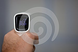 Non contact infrared forehead digital thermometer held by a young man with left hand with a defocused background. Close-up view