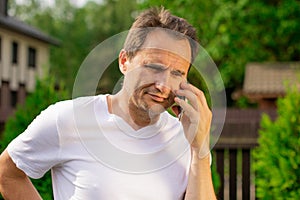 Non emotional portrait of unshaven 40s man in white T-shirt speaking on phone