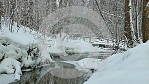 Non-freezing river with snowy banks in the winter forest. Snowfall.