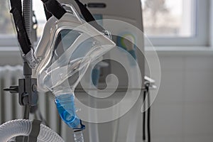 Non-invasive ventilation face mask, side view, on background medical ventilator in ICU in hospital