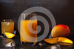 Mango Juice glass with whole and slices fruit on black dark background for veggie tables and healthy habits