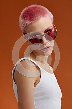 Nonconformist girl with pink short hairs with red sunglasses, over brown background photo