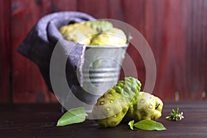 Noni fruit and leaves and noni in tank on wooden table.