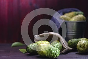 Noni fruit and leaves and noni in tank on wooden table.