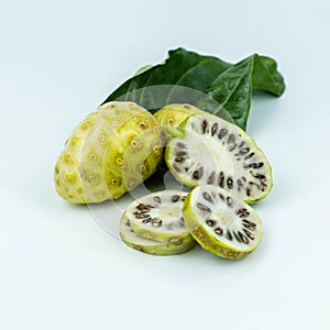 Noni or Morinda Citrifolia fruits with sliced and green leaf on white background