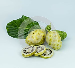 Noni or Morinda Citrifolia fruits with sliced and green leaf on white background