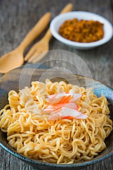 Noodle in ceramic bowl with crab stick on wooden background.