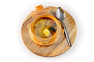 Noodle soup with chicken and quail egg in a pot on round wooden Board with a metal spoon top view, on white background