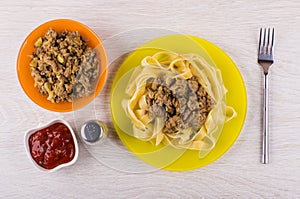 Noodles with fried mincemeat, bowls with ketchup, pepper, fork