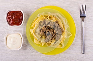 Noodles with fried mincemeat in plate, mayonnais and ketchup, fork