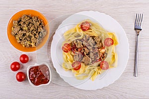 Noodles with fried mincemeat, tomatoes in plate, bowl with ketch