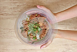 Noodles with pork and vegetables in take-out box on wooden table