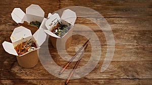 Noodles with pork and vegetables in take-out box on wooden table